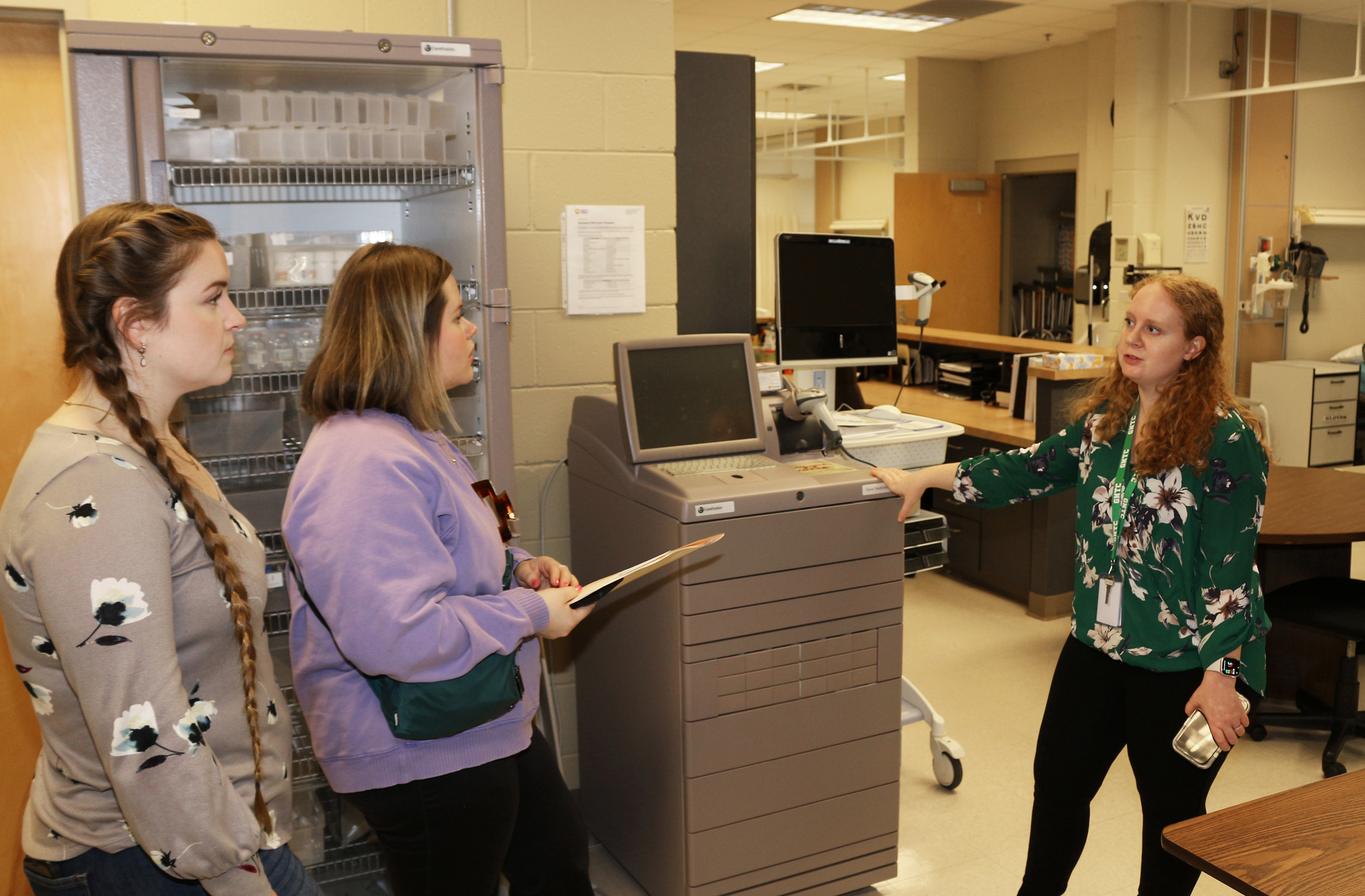 Lauren Vosika, 甜瓜app Practical Nursing instructor (right), explains to Audrey Powell (left) and Maleah Smith how the Pyxsis MedStation dispenses medication for patients.